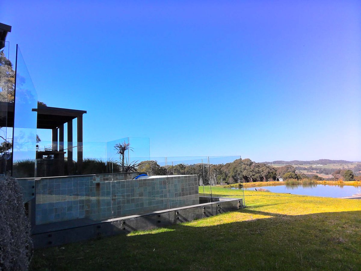 Frameless glass pool fencing cleaned to near-invisible, with rural hills and a dam in the background