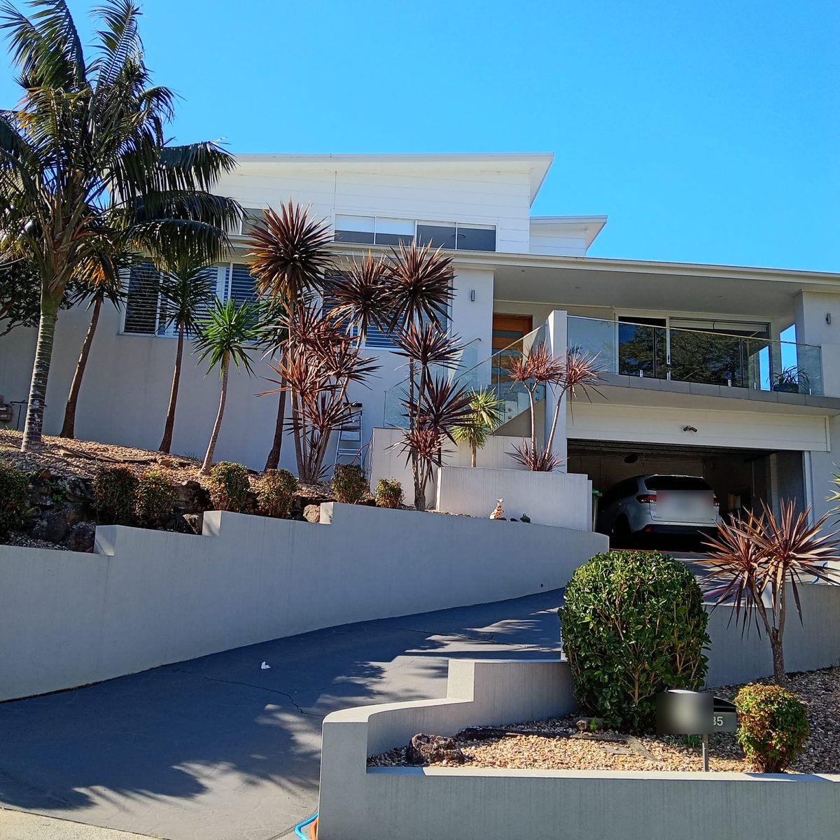 A modern two-storey Illawarra home with freshly cleaned windows and glass balustrade under a blue sky